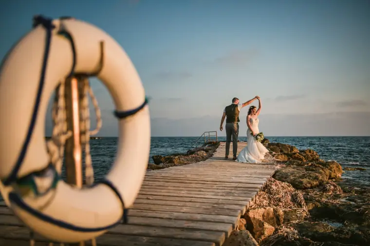 Couple dancing at the end of a wooden jetty by the sea, framed by a lifebuoy