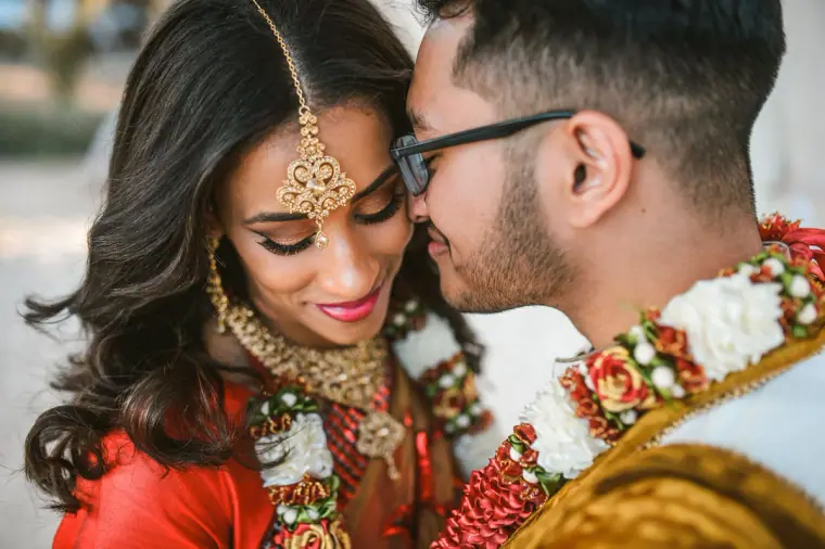 Groom nuzzling the bride's cheek as she smiles in her maang tikka and garland