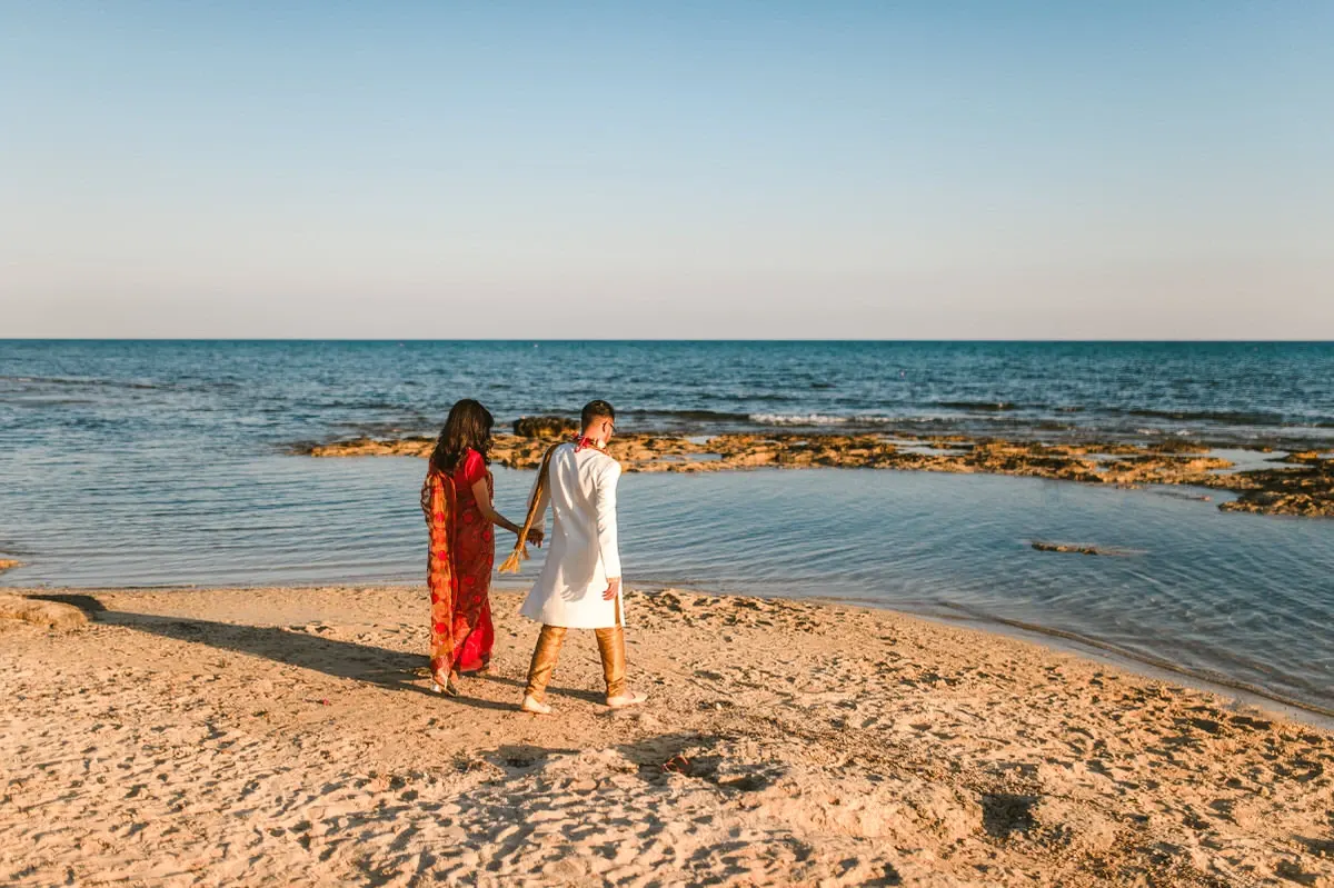 Couple in traditional dress walking hand in hand along the shoreline, Ayia Napa