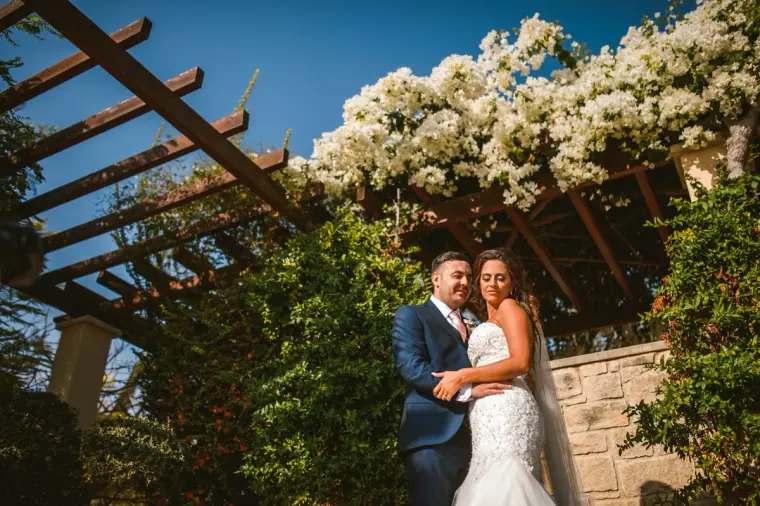 Erica and Harry beneath a white bougainvillea pergola at Aphrodite Hills, Paphos
