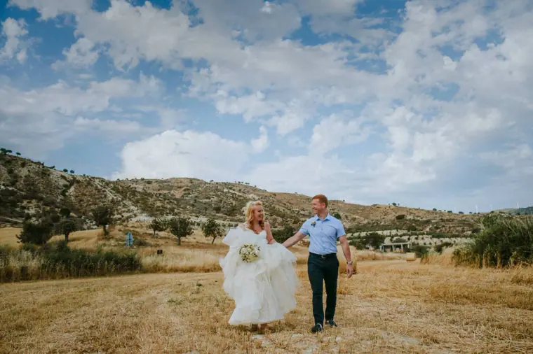 Couple walking across a dry field with rolling hills behind, near Vasilias Nikoklis Inn