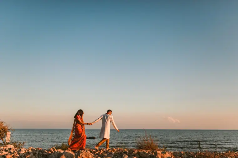 Couple in traditional dress walking hand in hand along the rocks above the sea