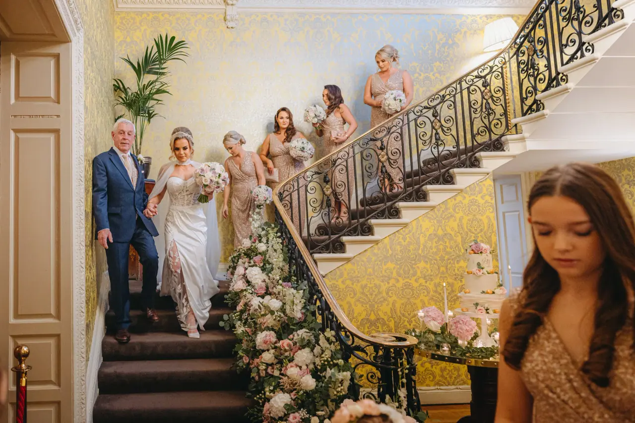 Jade descending Hedsor House's sweeping staircase with her father, bridesmaids following