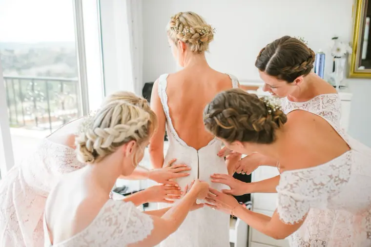 Bridesmaids with braided hair fastening the back of Rachel's lace gown, Pissouri