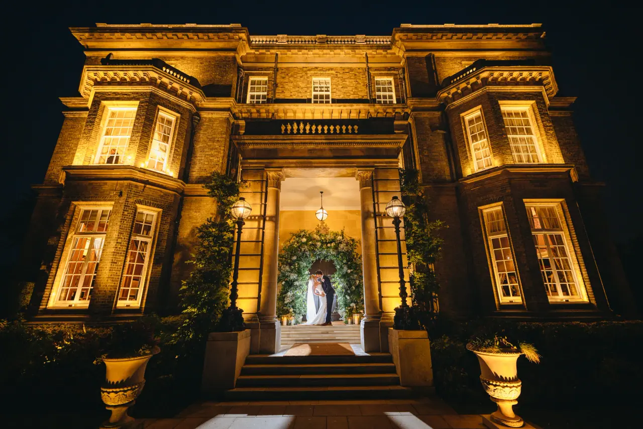 Hedsor House glowing at night with Jade and Ian framed in the lit doorway