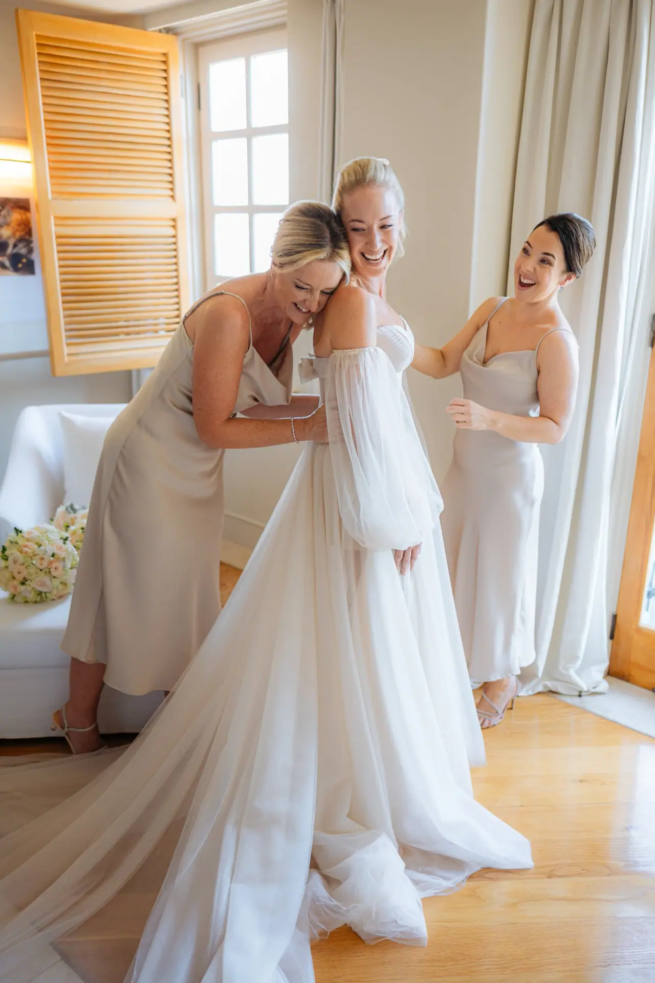 Bridesmaids helping Jade into her gown in a bright room at Anassa