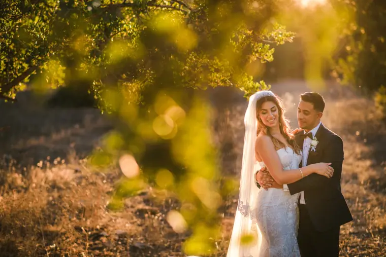 Couple embracing in golden backlight seen through blurred leaves, Anassa