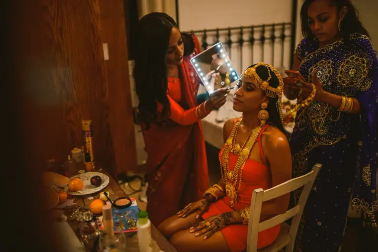 Bride in gold jewellery seated in the villa as women prepare her for the evening ceremony