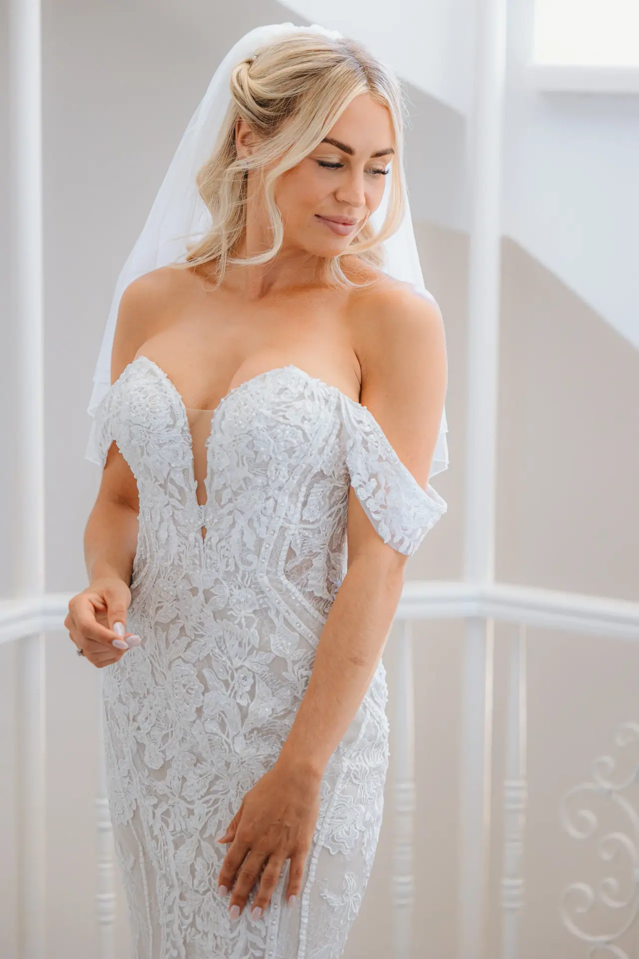 Jayley in an off-the-shoulder lace gown and veil, eyes lowered, at Alassos