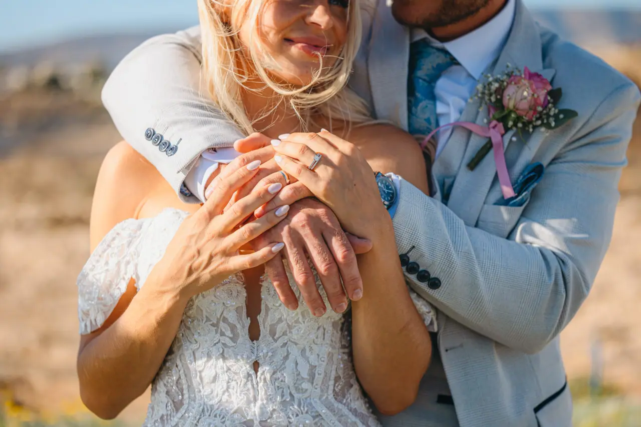 Close-up of Jayley's hands and wedding rings on Nick's arm as they embrace