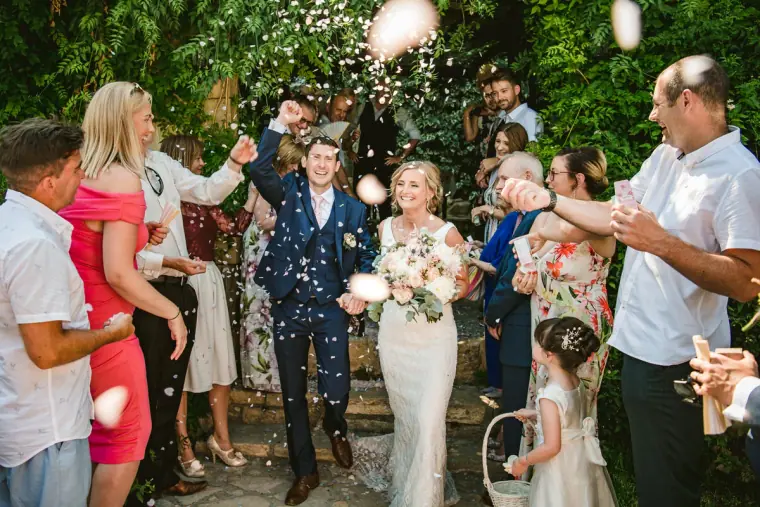Bride and groom walking through a shower of confetti and petals thrown by guests