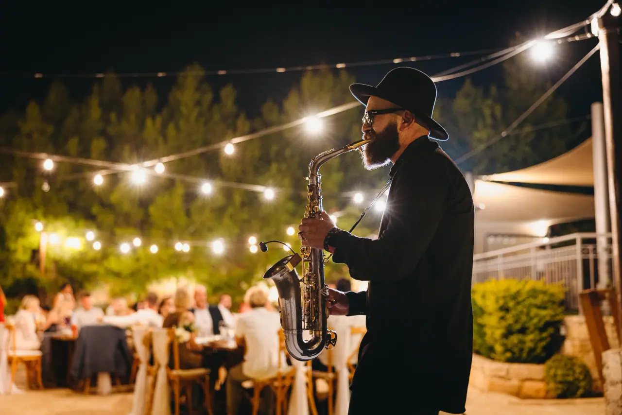 Saxophonist playing at a night reception under festoon lights at Liopetro