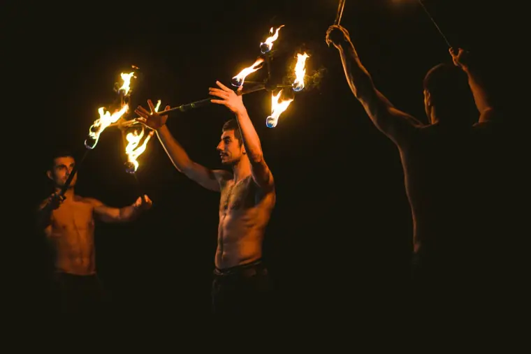 Shirtless fire dancers twirling flaming staffs at night
