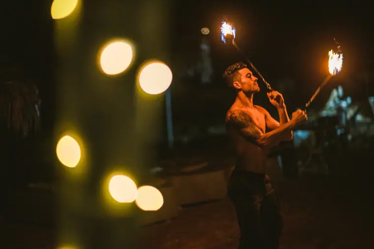 Fire performer holding two flaming torches behind glowing bokeh lights