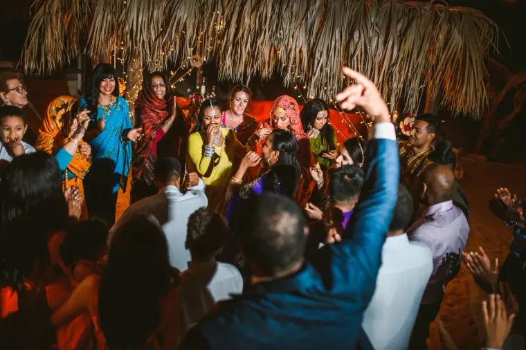 Guests cheering and clapping around the dance floor beneath the thatched canopy at night