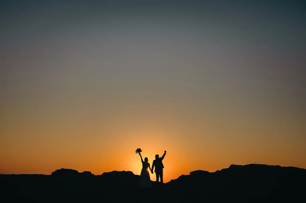 Liv and Jacq silhouetted on a hilltop at sunset, arms raised