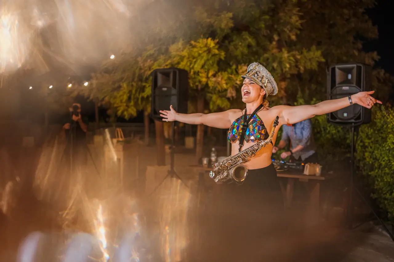 Saxophonist in a sequinned headdress playing with arms outstretched on the dancefloor
