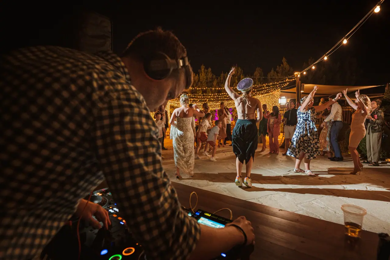 DJ in headphones as guests dance under festoon lights at Liopetro