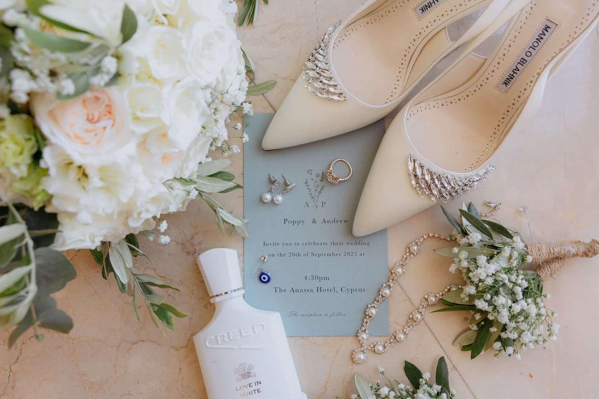 Bridal shoes with crystal buckles, perfume, rings and invitation among white roses