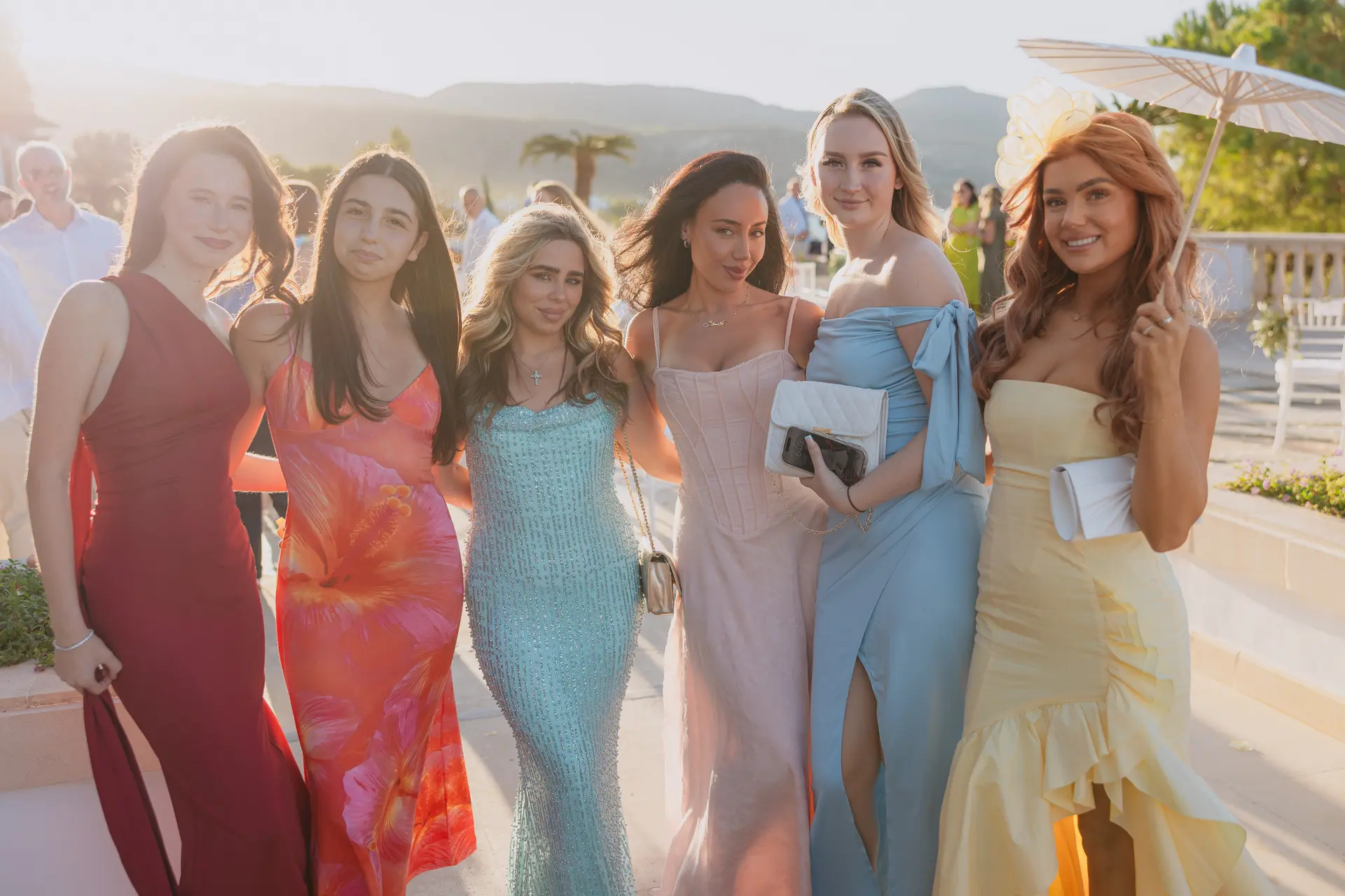 Group of guests in colourful dresses posing in the sunshine at the cocktail hour