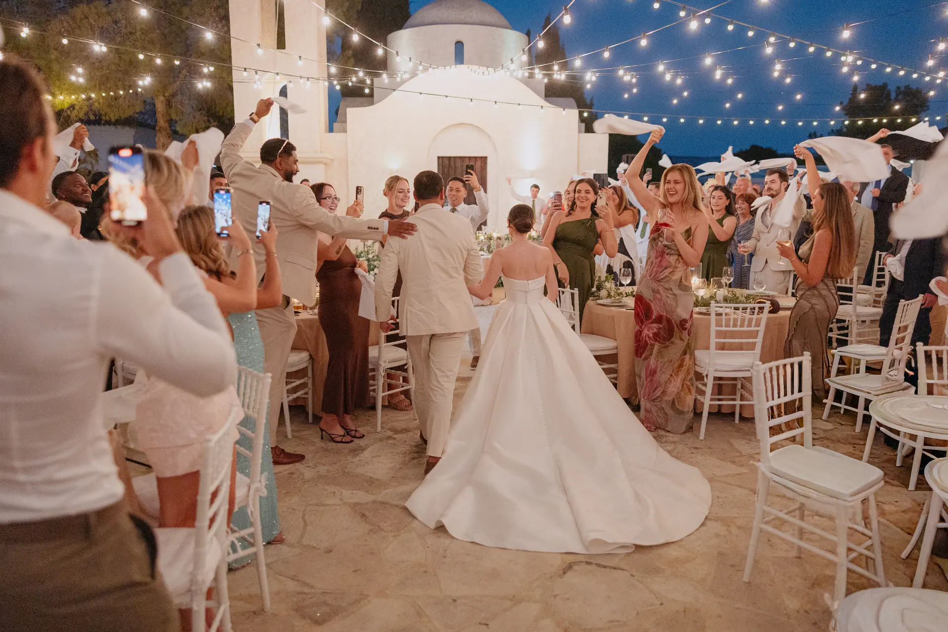 Bride arriving at the reception as guests film and cheer beside the chapel