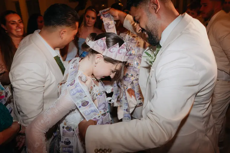 Poppy in a banknote crown surrounded by Andrew and groomsmen during the money dance
