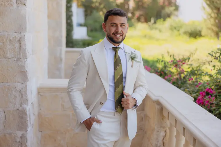 Andrew in his cream suit and green tie on a balcony at Anassa