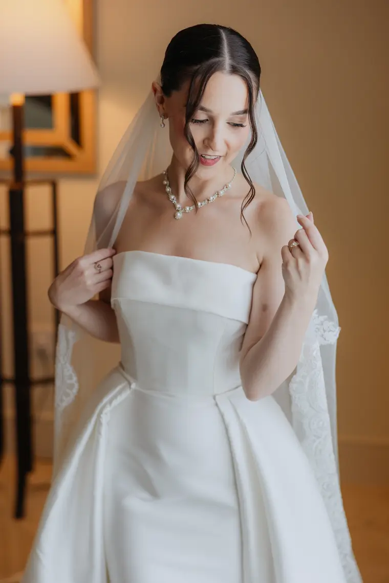 Poppy smiling as she holds her veil, dressed in her strapless gown