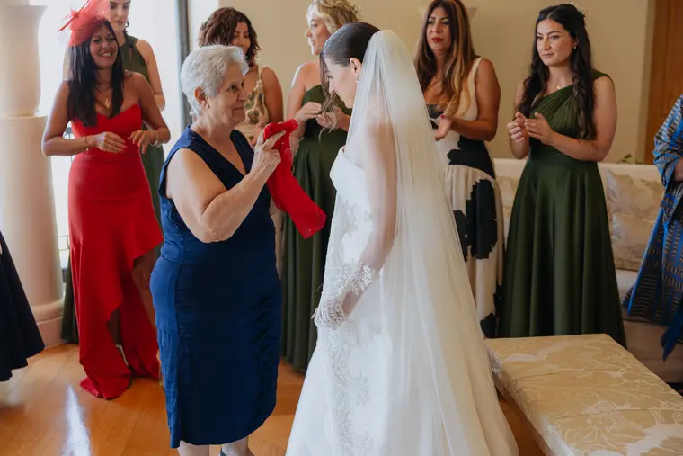Older woman holding a red ribbon beside the bride during the blessing