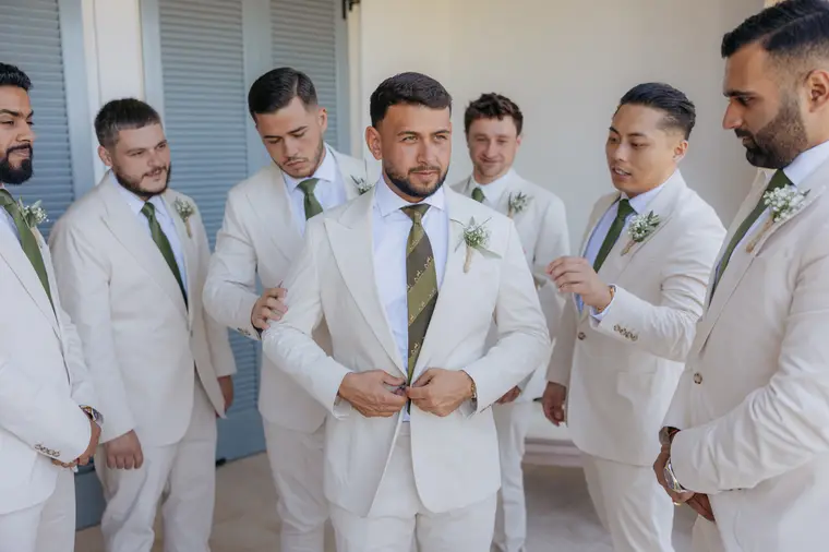 Groomsmen in cream suits helping Andrew with his jacket
