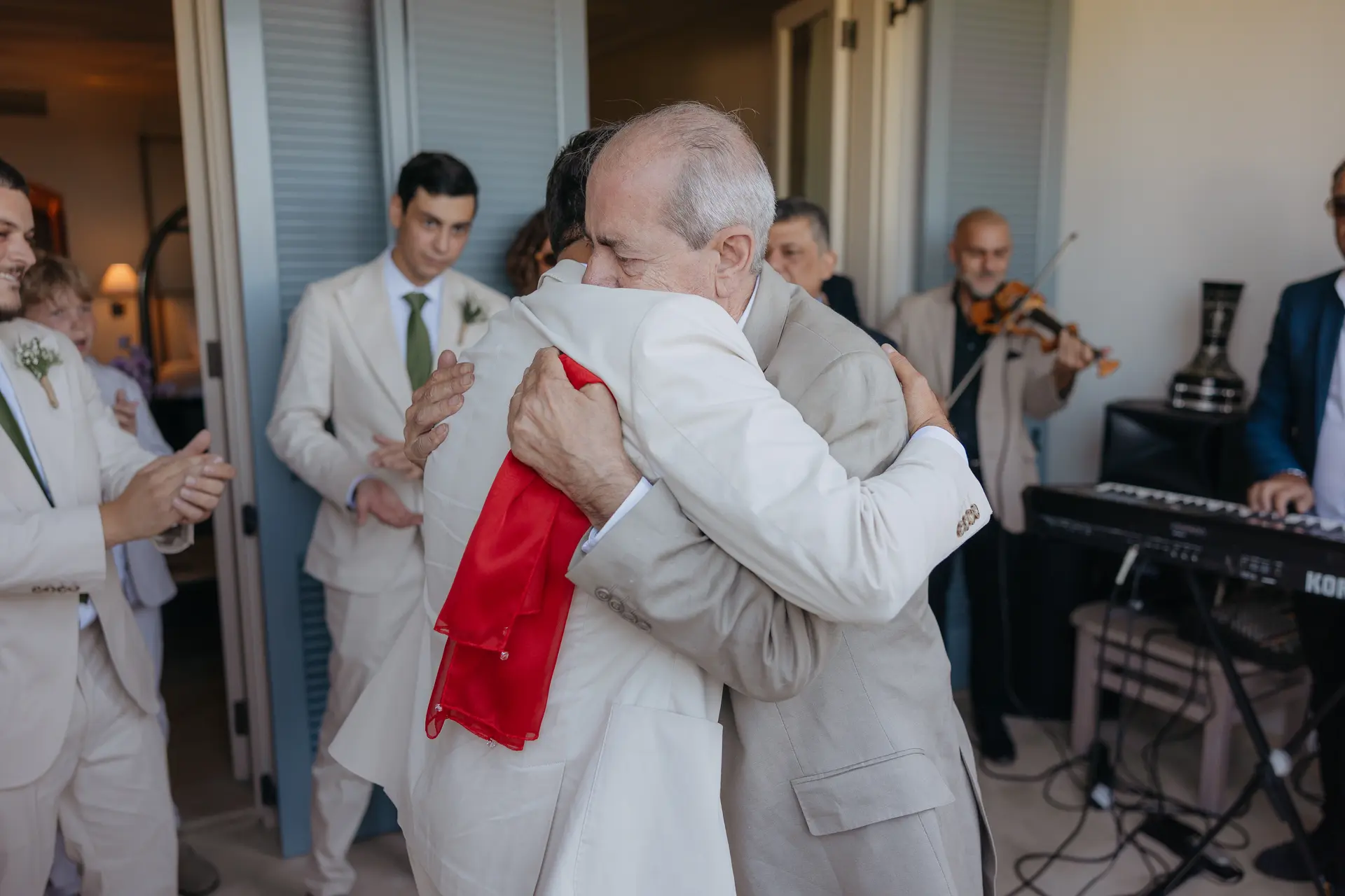 Andrew embraced by an older man, a red ribbon draped across his back