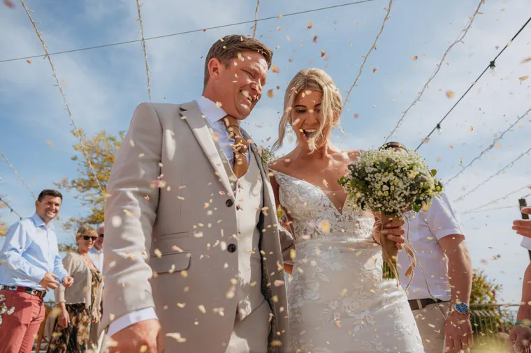 Bride and groom laughing under falling confetti with guests at Liopetro, Kouklia