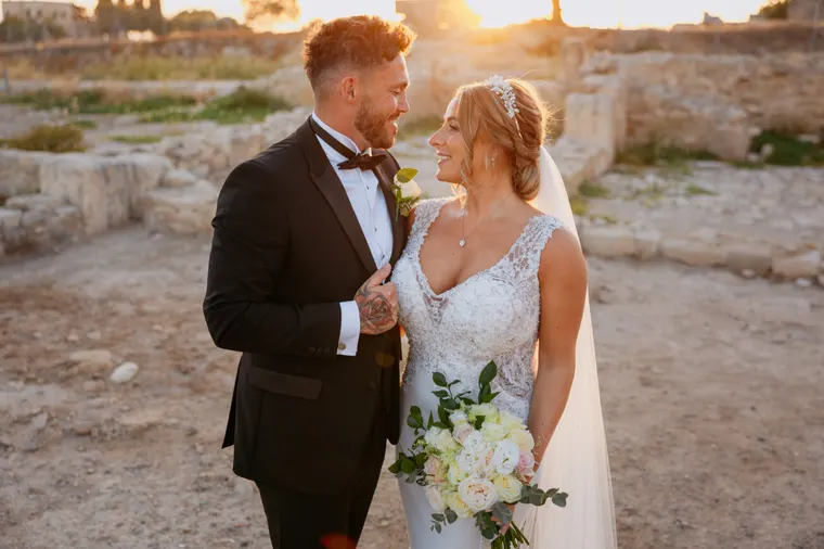Bride and groom smiling at each other among ancient ruins at sunset, Kouklia