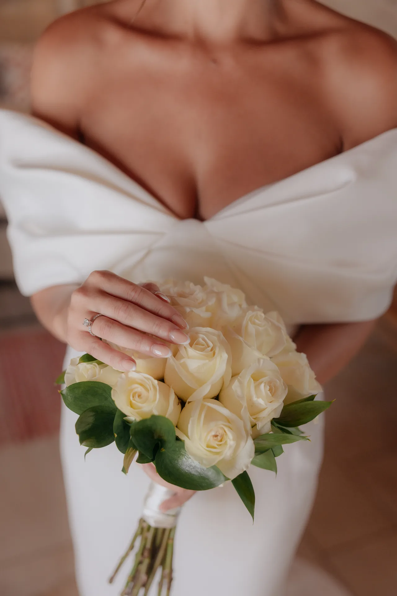 Close-up of the bride holding a bouquet of ivory roses against her off-shoulder gown