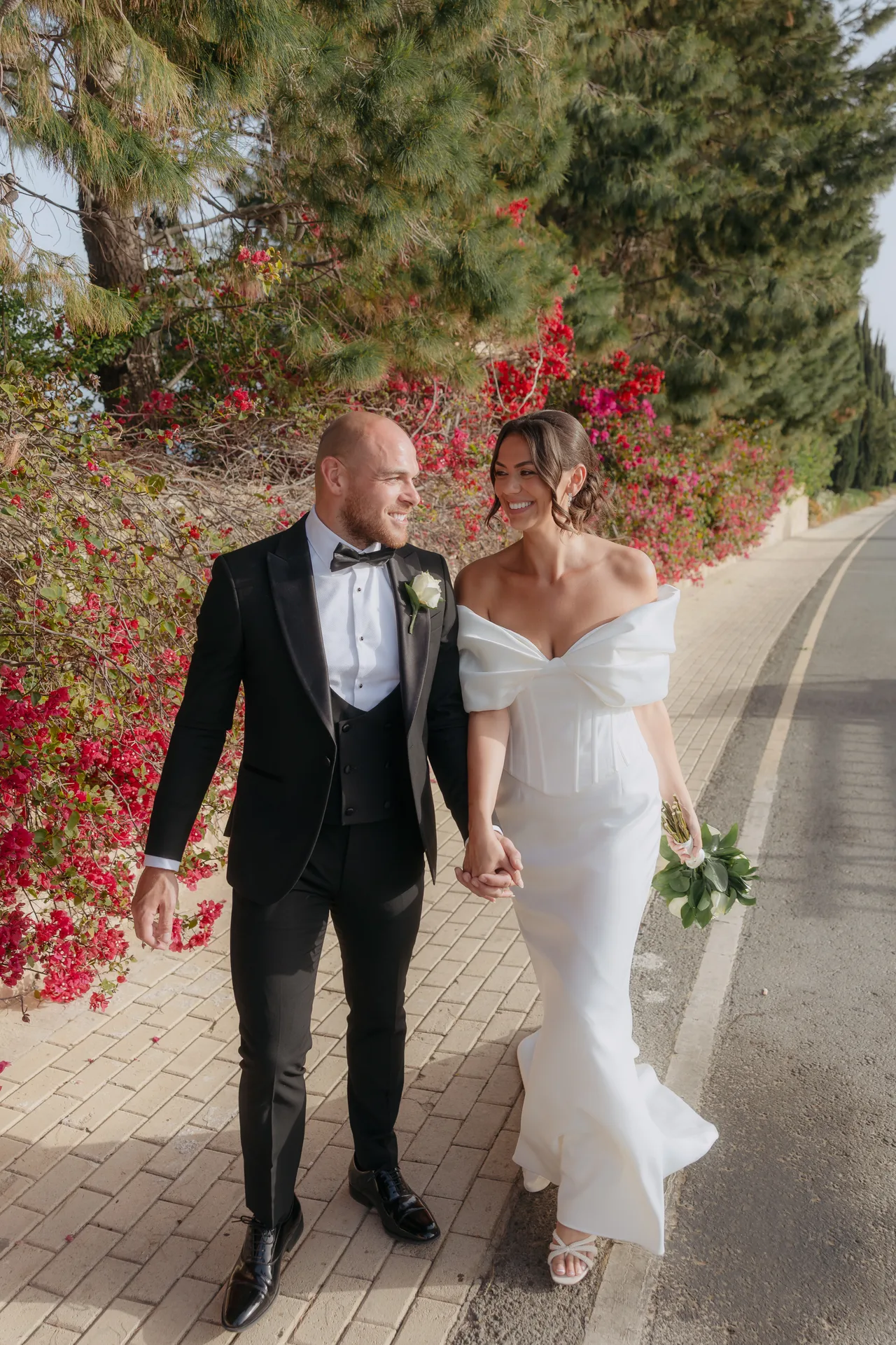 Bride and groom laughing hand in hand beside pink bougainvillea near Liopetro, Kouklia