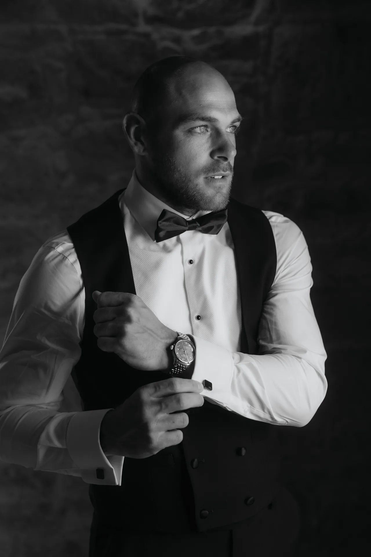 Black-and-white photo of the groom in a bow tie fastening his cufflinks