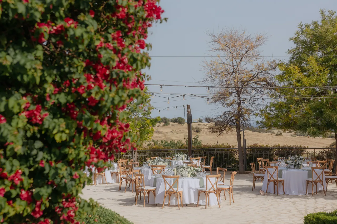 Reception tables on the terrace beyond red bougainvillea, coast in the distance, Liopetro